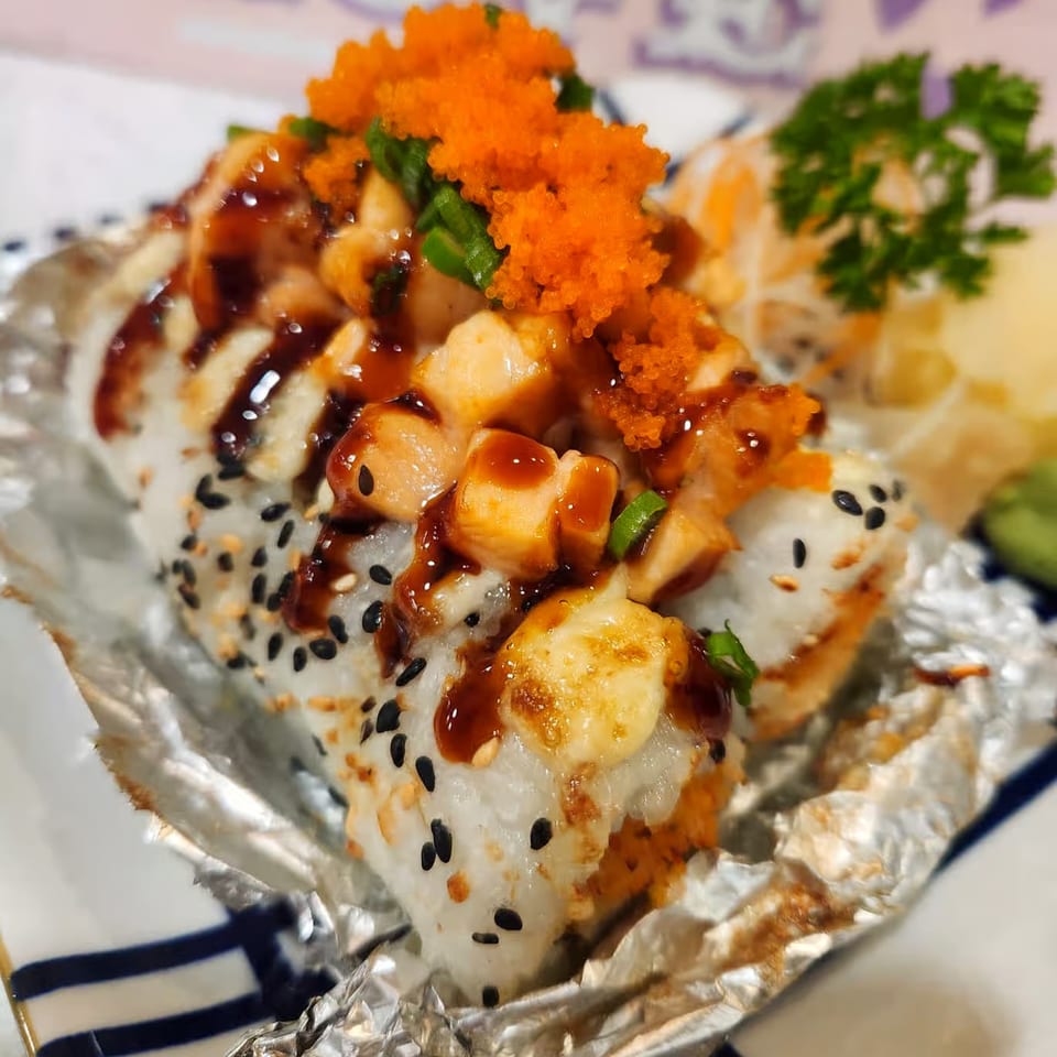 Close-up of sushi rolls topped with orange roe, sauce, and green onions, served on foil.