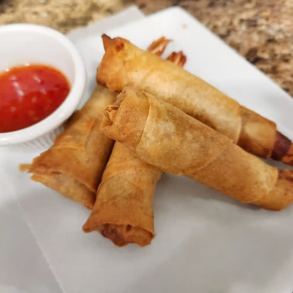 Golden-fried shrimp spring rolls with a side of sweet chili dipping sauce on a white plate.