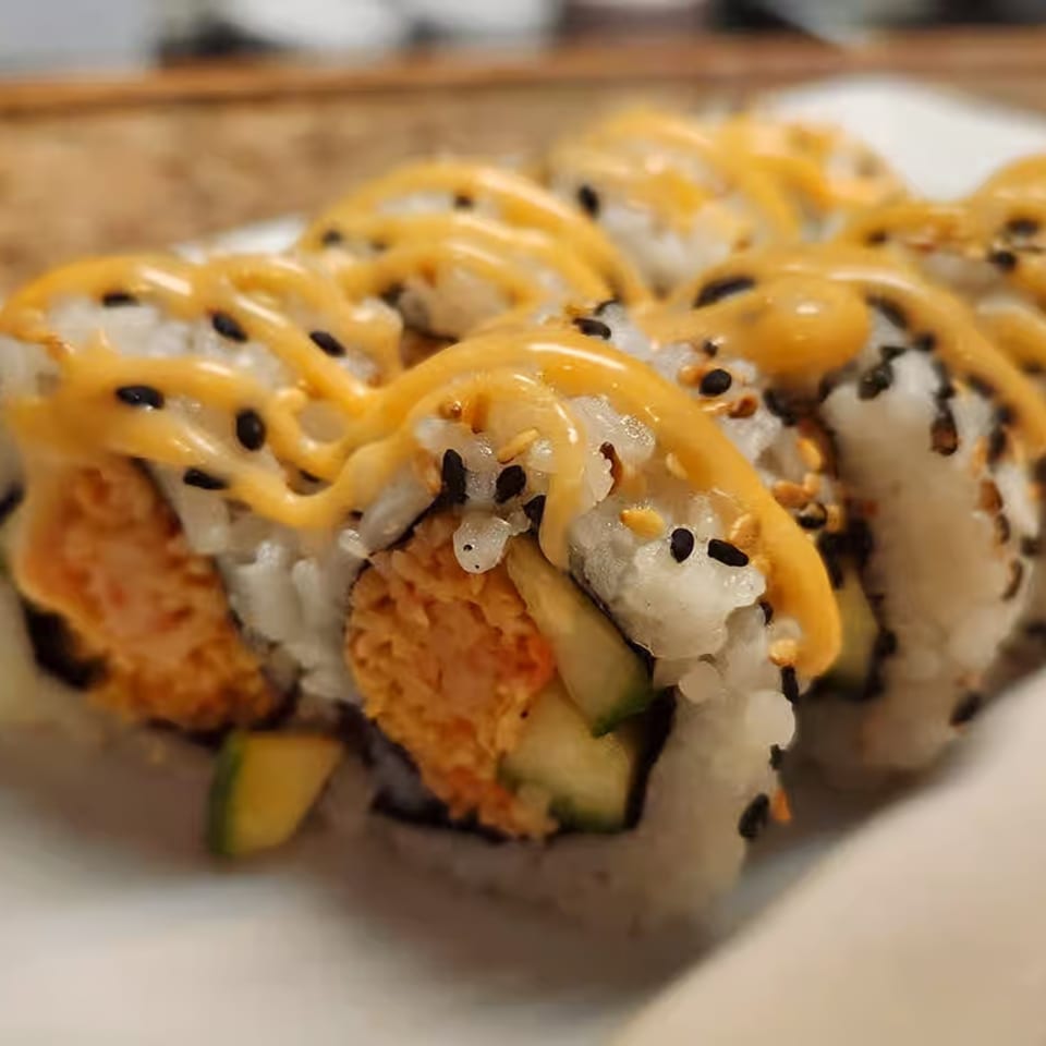 Close-up of Honey's Bie Thai & Sushi's spicy tuna rolls with avocado, topped with orange sauce and sesame seeds.