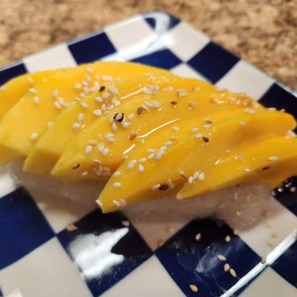 Sweet mango slices with sesame seeds on sticky rice, served on a blue and white checkered plate.