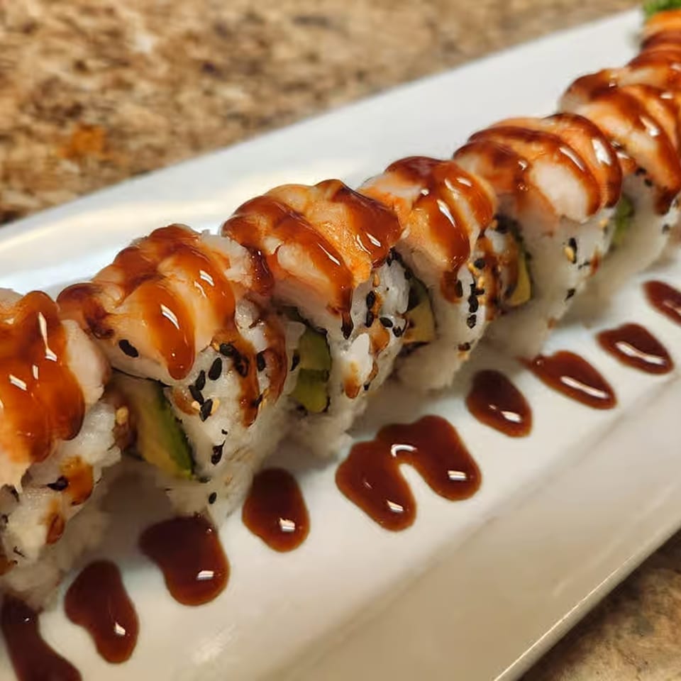 A row of sushi rolls with shrimp, avocado, sesame seeds, and a sweet brown sauce.